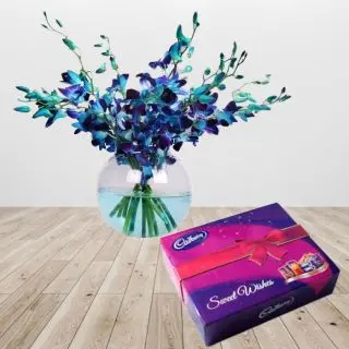 8 blue orchids arranged in a glass vase with box of celebration chocolates 