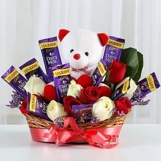 Basket arrangement of 10 red and white roses, 10 dairy milk chocolates, with 6 inch teddybear sitting in it 