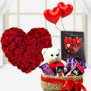 Heart shape arrangement of 50 red roses with a cute teddybear sitting in basket of assorted chocolates with greeting card and pair of heart shape balloons