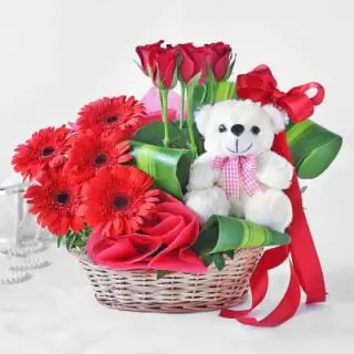 cute 6 inch teddybear sitting in a basket of 12 red gerberas 